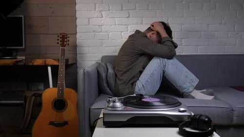 Man Covering His Face with Hands Sitting on a Sofa in a Living Room Experiencing Mental Health
