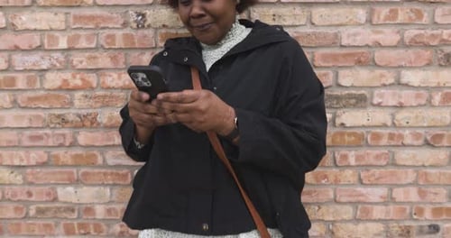 Smiling Woman Uses Phone by a Brick Wall