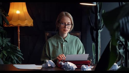woman in a green shirt sits at a table in her cozy home, typing a novel on a vintage typewriter