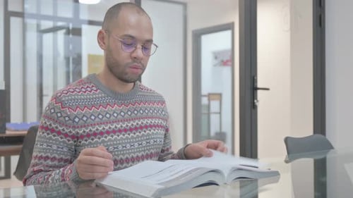 Young Hispanic Man Reading Book in Office