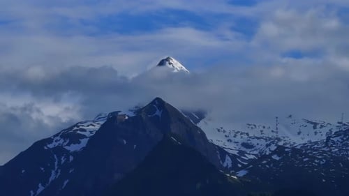 Above the clouds, top of majestic mountain covered in snow and ice. Aerial