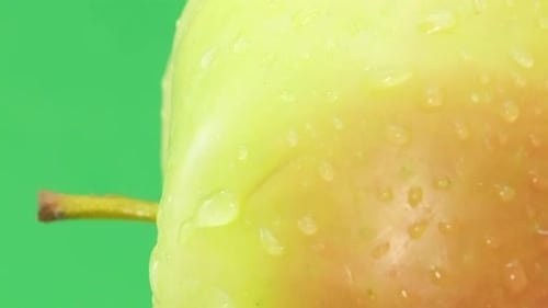 A Ripe Apple in a Raindrop Rotates on a Green Background Vertical Video