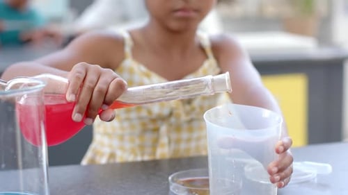 In a school classroom setting, a young biracial girl conducts a science experiment
