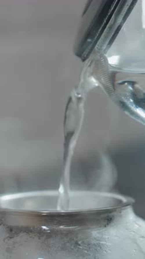 Close Up of Pouring Hot Water Into Glass Kettle with Metal Filter and Steam Rising