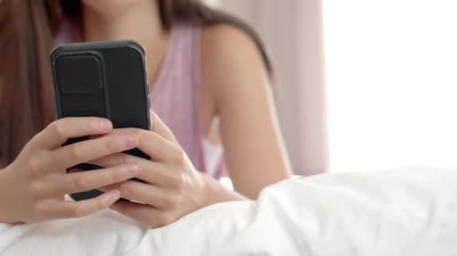 Teenage Caucasian girl with brown hair is using a smartphone in bed at home