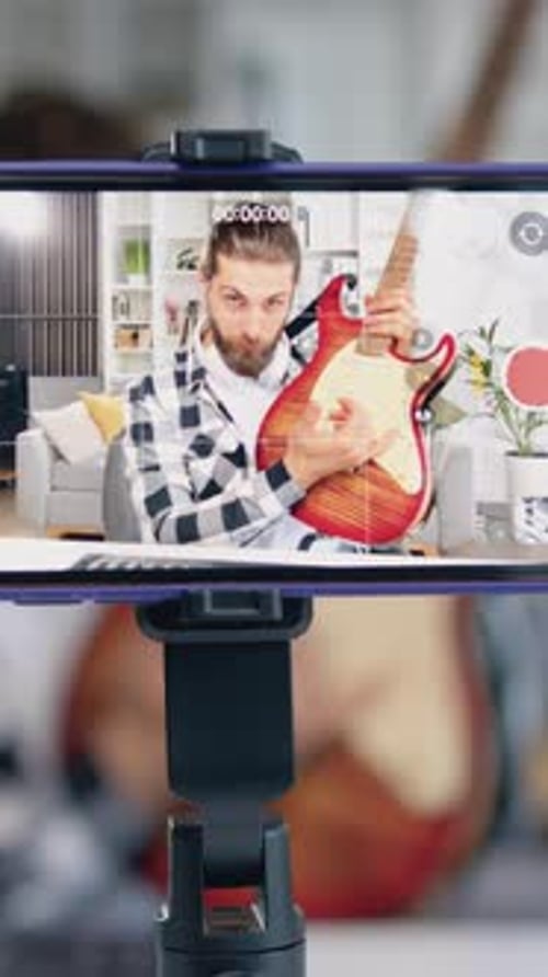 Young Man Plays Guitar for Phone Recording Indoors