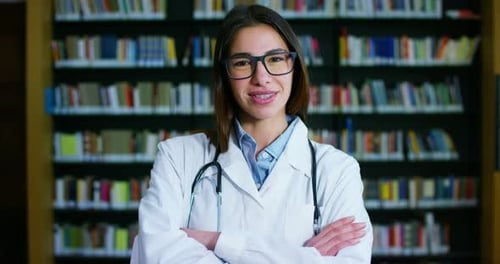 Una joven y hermosa doctora en una biblioteca sonriendo feliz y sosteniendo libros después de hacer un mar