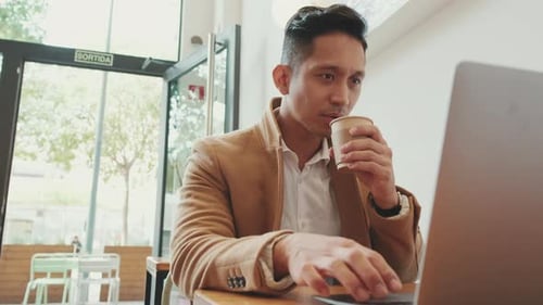 Young handsome businessman is working with laptop in cafe with cup of coffee in his hand
