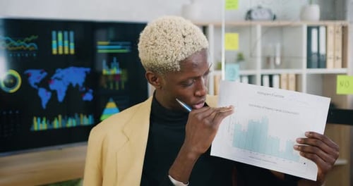 African man talking and showing sheet of paper with graphs for colleagues looking at laptop