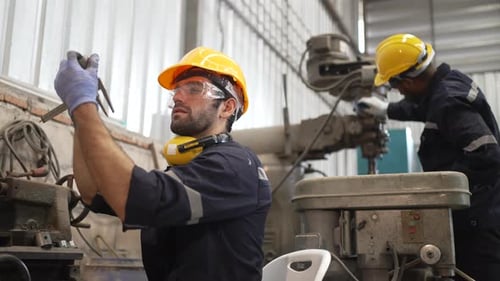 Blue collar workers at machine shop with welding robot arm.