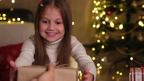 Excited Girl Receiving Christmas Gift by Glowing Tree
