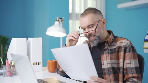 Man Reads Documents at Desk Happy with the Result