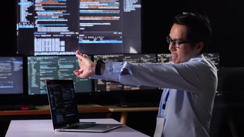 Programmer Stretching While Writing Code By A Laptop Using Multiple Monitors Showing Database