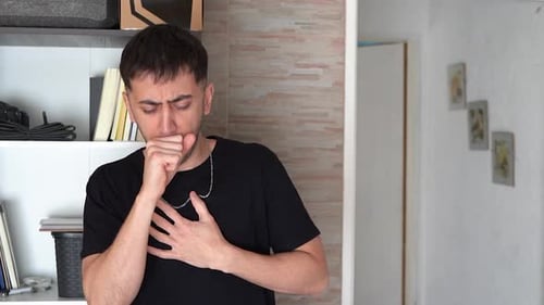 Young man at home feeling unwell and suffering from apparent chesty cough