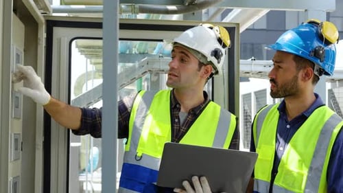 Two engineers in safety uniform checking building exterior power system at construction site rooftop