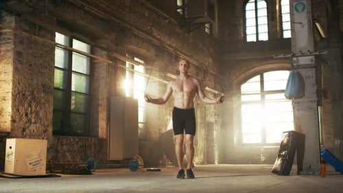 Muscular Fit Man Exercises with Jump Skipping Rope in a Deserted Factory Hardcore Gym. He's Sweat