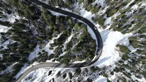 Snowy mountain road with cars driving through a forest in a scenic winter landscape, aerial view