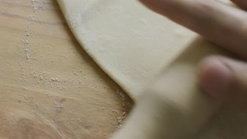 Rolling Pin Flattens Dough on Wooden Surface