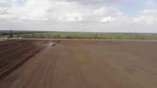 Blue tractror planting sunflower with yellow planter on the cultivated field in Ukraine