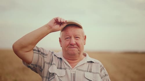 Portrait Happy Senior Man Farm Worker Looking at Camera Touching Hat on Wheat Field in Summer