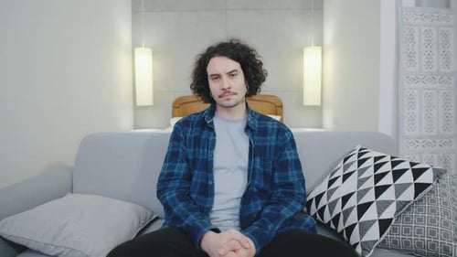 El hombre se sienta tranquilamente en un sofá en una habitación moderna y bien iluminada con una decoración neutra que se centra en la relajación y