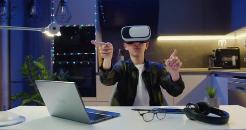 Niño adolescente con gafas de realidad virtual que mueve las manos en el aire, se desplaza y escribe, sentado en el escritorio de la sala de estar.