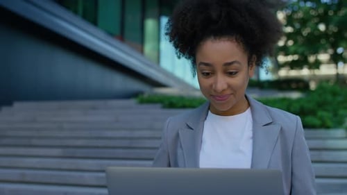 Businesswoman Working on Laptop Outside Modern Office Building