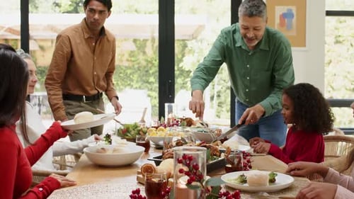 Família extensa comemorando a refeição natalina esculpindo perus passando pãezinhos servindo salada na mesa de jantar