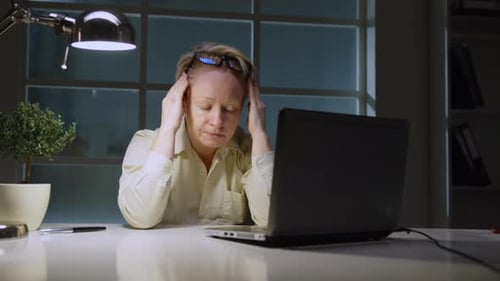 Woman manager rubs her eyes from fatigue when working on laptop in office late in evening