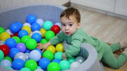 Lovely kid plays at the dry pool filled with colorful toys. Small child plays indoors. Top view.