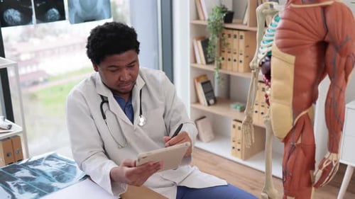 Doctor Writing on Tablet While Pointing at Skeleton