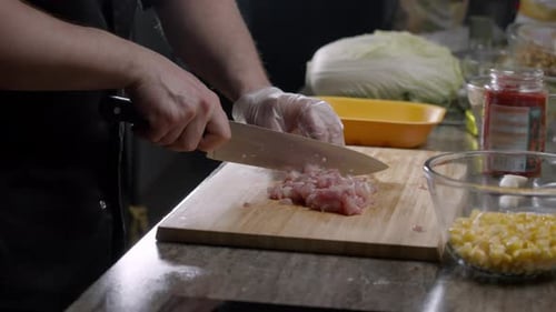 Cook schneidet geschickt rohe Hähnchenfilets auf einem Schneidebrett
