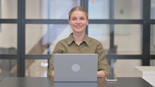 Mature Adult Woman Smiling at Camera while Working on Laptop in Office