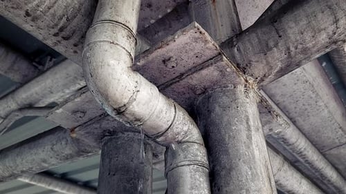 Industrial pipe joint under concrete structure showing leakage and wear
