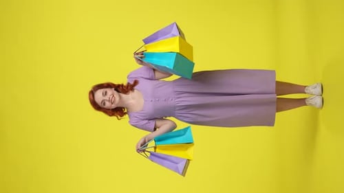 Redhaired Woman Demonstrates Colorful Shopping Bags Full Length Woman in the Studio on a Yellow