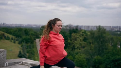 Im Park: Junges Mädchen in einem orangefarbenen Hoodie wärmt sich auf, gesunder Lebensstil, meditative Stände
