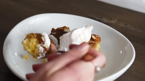 Female Hand With Spoon Eating A Slice Of Banana Caramel Cake With Frosting. close up