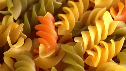 Multicolored italian pasta Fusilli or Rotini rotating in macro background top view. Durum wheat