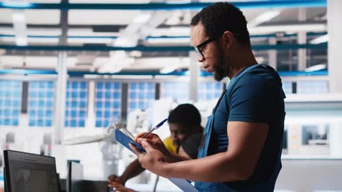 Black Engineer in Photovoltaics Factory Reviews Performance of Solar Panels
