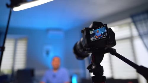 Camera on tripod taking video of a man shown on the display. Low angle view.