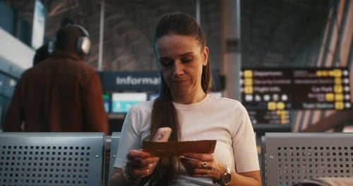 Focused Woman Sitting in Terminal Seating Area and Using Phone for Check in