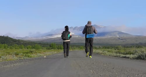 Pareja caminando con mochilas en una carretera con montañas de fondo Dovrefjell Sunndalsfjella