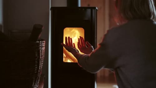 Woman is warming up by the traditional wood-burning fireplace. Burning fire for the cosy evening.