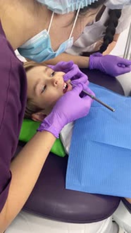 A Doctor Dentist in a Medical Mask and Purple Rubber Gloves Puts a Seal on a Little Boy Toddler