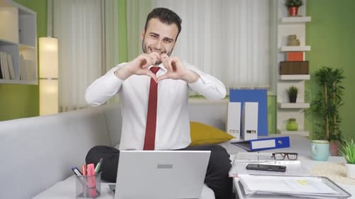 Man Making Heart Shape on Couch With Laptop
