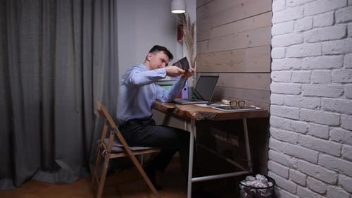 Mann in einem hellblauen Hemd sieht überrascht und verärgert aus, während er eine leere Brieftasche hält und an einem sitzt