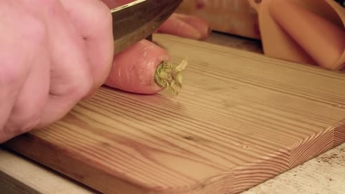 Low angle close up: Chopping raw carrots on wooden cutting board