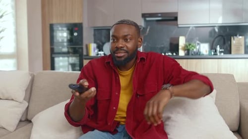 Excited Emotional Afroamerican Guy Turning on TV Choosing His Favorite Channel on Remote Control