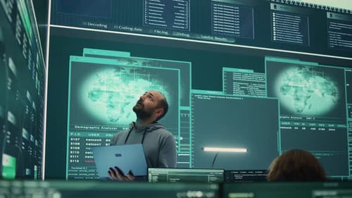 Governmental Hacker Examines Info on a Big Screen in Agency Office