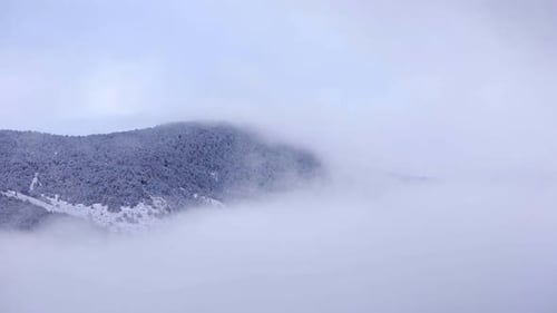 TIMELAPSE - Snowed mountains getting covered by fog.